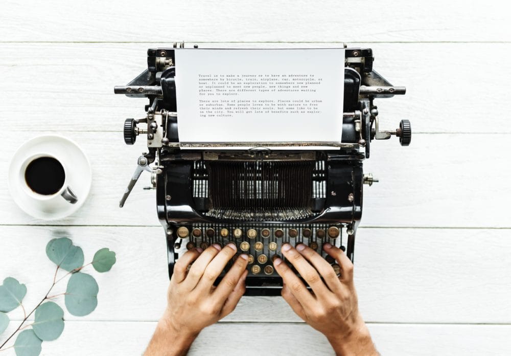 Hands using typewriter on a table with a coffee pot