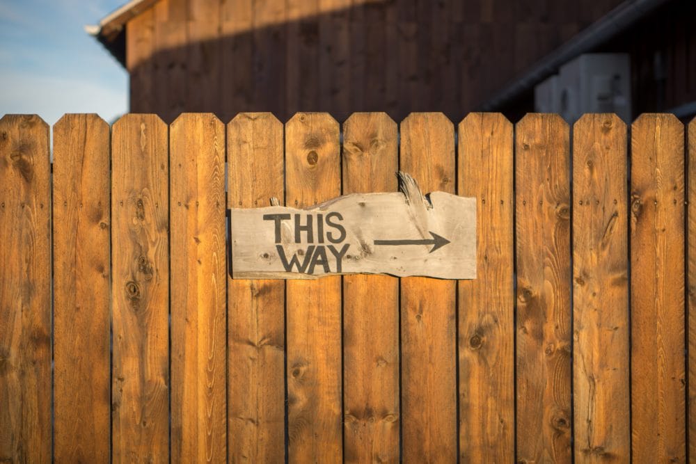 "This way" written on wooden fence with arrow pointing right